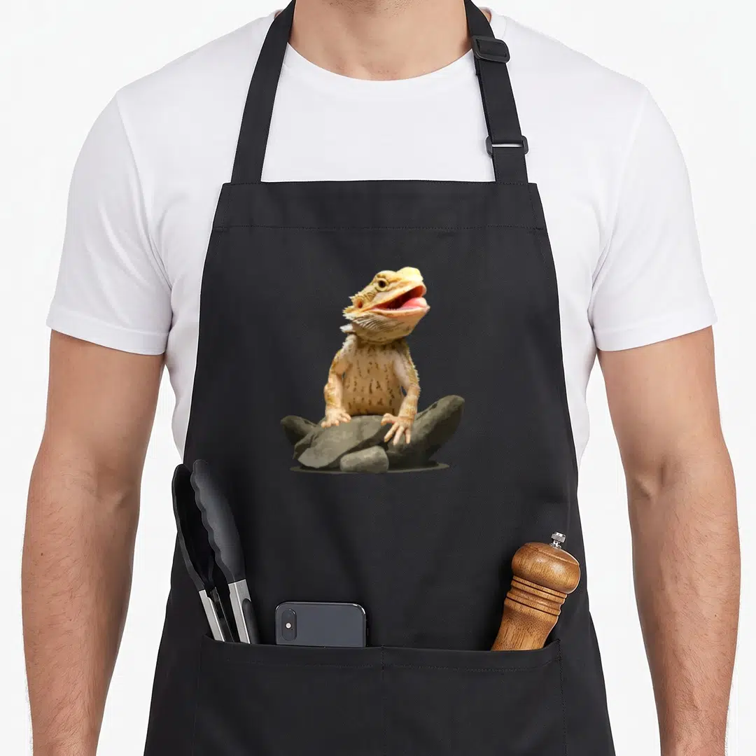 Gecko dragon apron - Bearded dragon with open mouth sitting on grey rocks in tan and beige photo style — shown on a black cotton canvas apron against a white background