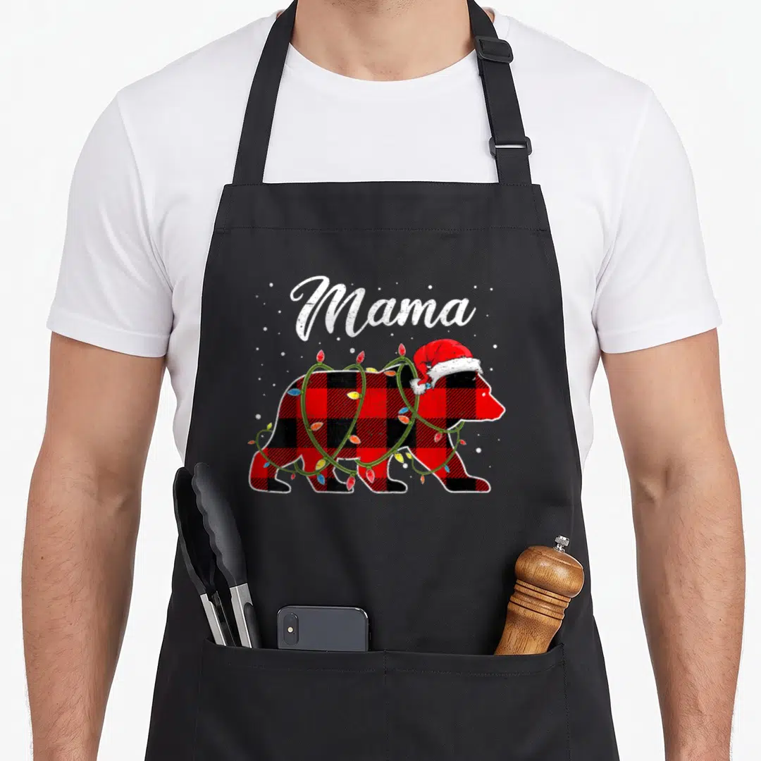 Bear red plaid apron - Mama text above cartoon bear in red plaid wearing Santa hat and Christmas lights — shown on a black cotton canvas apron against a white background