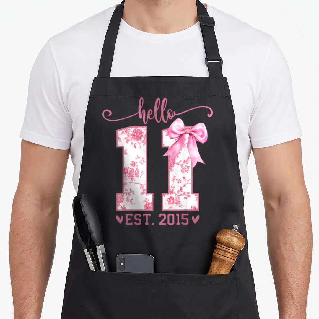 Coquette birthday apron - Pink floral number 11 with bow and EST 2015 text — shown on a black cotton canvas apron against a white background
