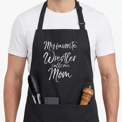 Wrestler mother's apron - White stacked script text reading My favorite Wrestler calls me Mom — shown on a black cotton canvas apron against a white background