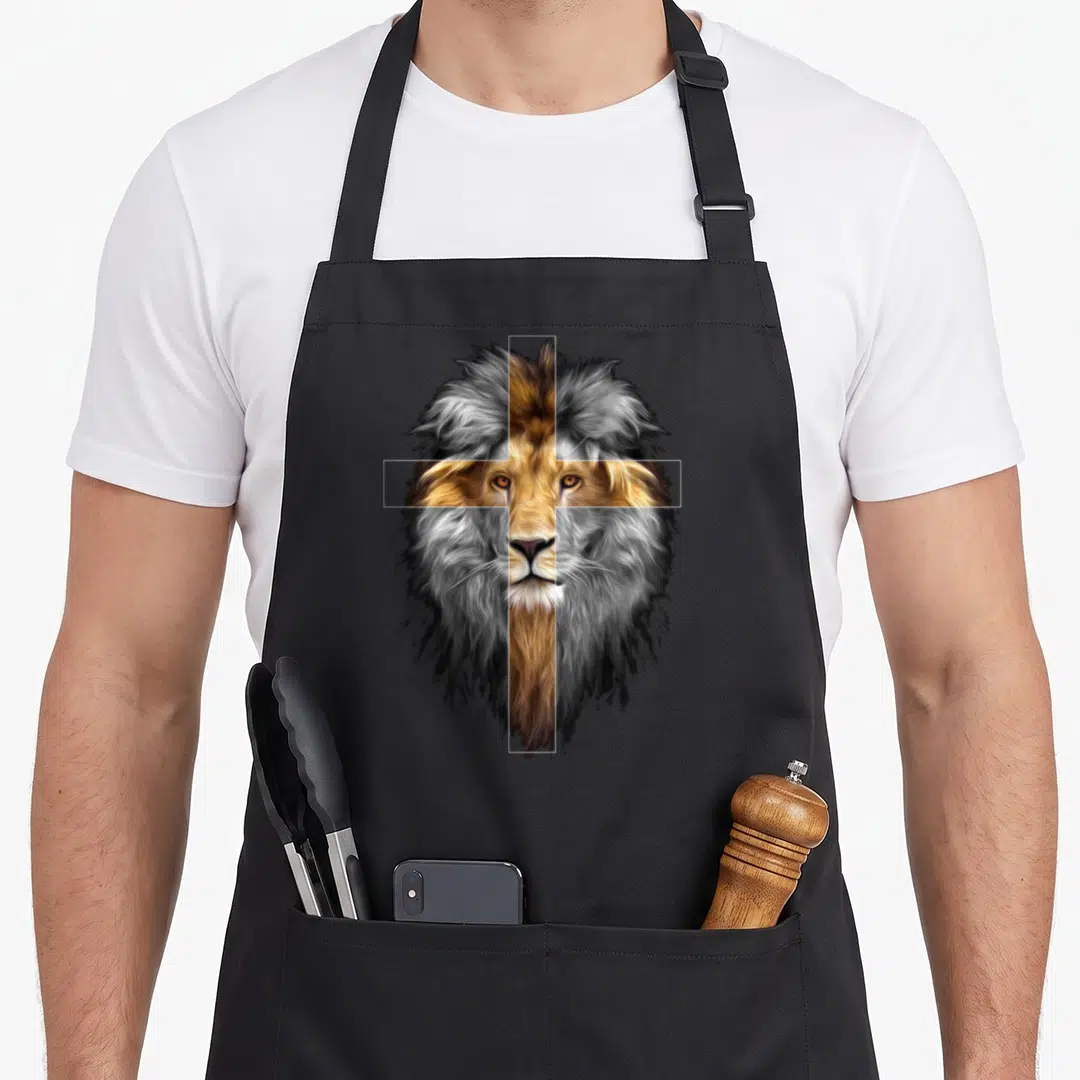 Jesus judah lions apron - Realistic lion head with white cross outline in brown and grey tones — shown on a black cotton canvas apron against a white background
