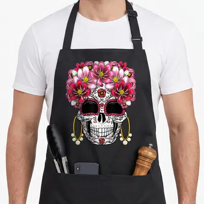 Muerto day of the dead apron - Decorated skull with pink red flowers and gold hoop earrings with pearls — shown on a black cotton canvas apron against a white background