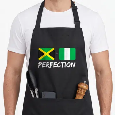 Nigerian heritage aprons - Two flags with plus sign and PERFECTION text in green yellow white black — shown on a black cotton canvas apron against a white background