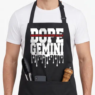 Decor king apron - White text DOPE UNAPOLOGETICALLY GEMINI with red accent and dripping paint effect at bottom — shown on a black cotton canvas apron against a white background