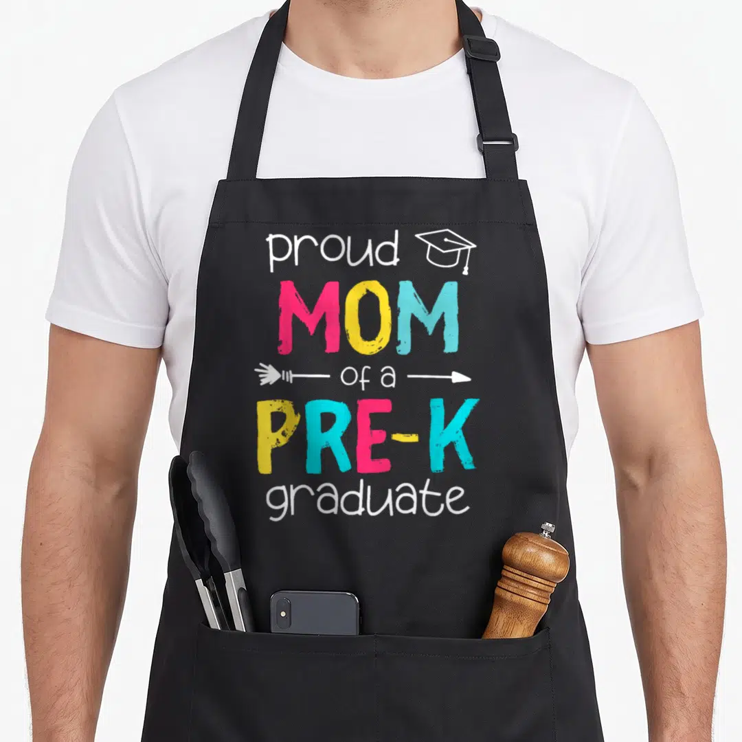 Prek mother's apron - Stacked colorful text reading proud MOM of a PRE-K graduate with cap and arrow graphics — shown on a black cotton canvas apron against a white background
