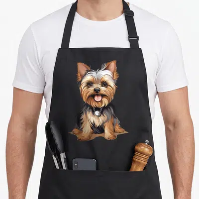 Yorkshire top dog aprons - Cartoon Yorkshire Terrier sitting in tan, black, grey, and silver with a silver collar tag — shown on a black cotton canvas apron against a white background