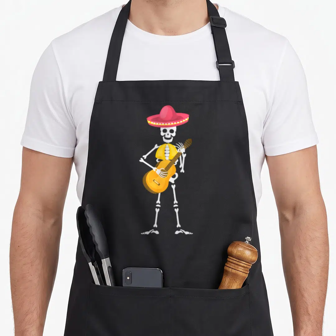 Hat mexican apron - Cartoon skeleton in pink sombrero and yellow vest playing guitar — shown on a black cotton canvas apron against a white background