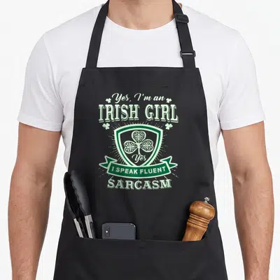Perfect irish aprons - Green shamrock shield with Yes I Speak Fluent Sarcasm typography and banner — shown on a black cotton canvas apron against a white background