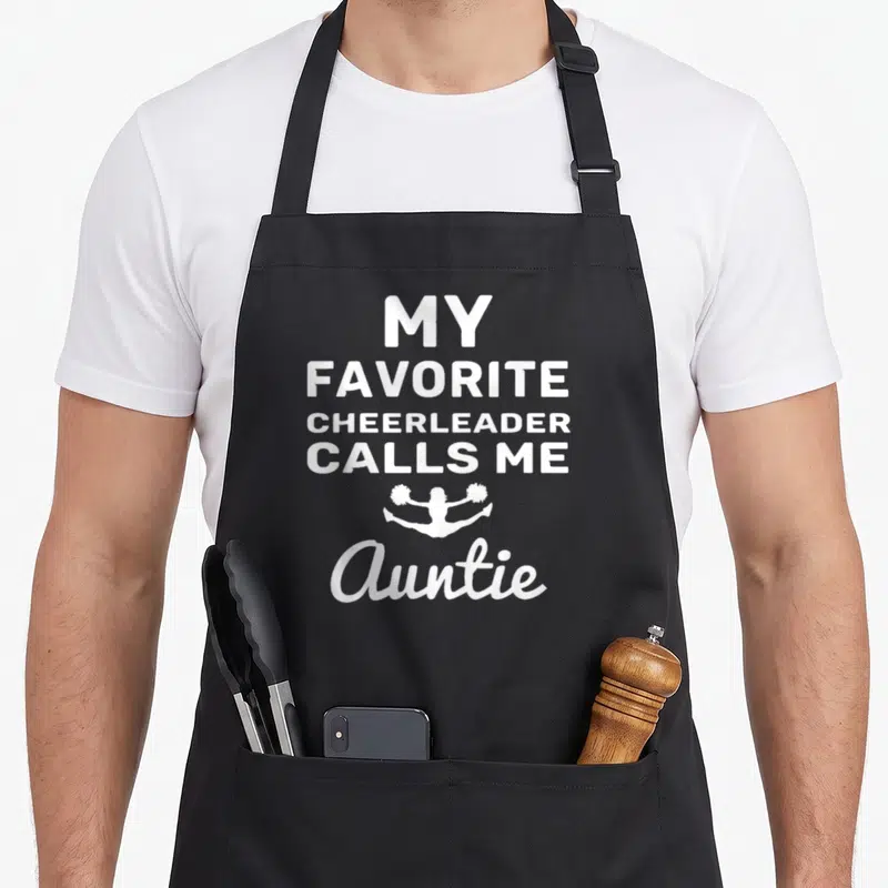 Cheerleader cheerleading mom apron - White stacked text reading My Favorite Cheerleader Calls Me Auntie — shown on a black cotton canvas apron against a white background
