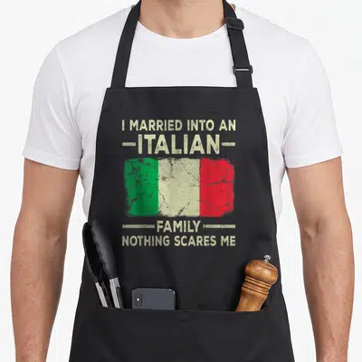 Married italian apron - Distressed Italian flag with beige text I MARRIED INTO AN ITALIAN FAMILY NOTHING SCARES ME — shown on a black cotton canvas apron against a white background