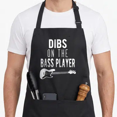 Dib bassist apron - White DIBS ON THE BASS PLAYER text stacked above a bass guitar silhouette — shown on a black cotton canvas apron against a white background