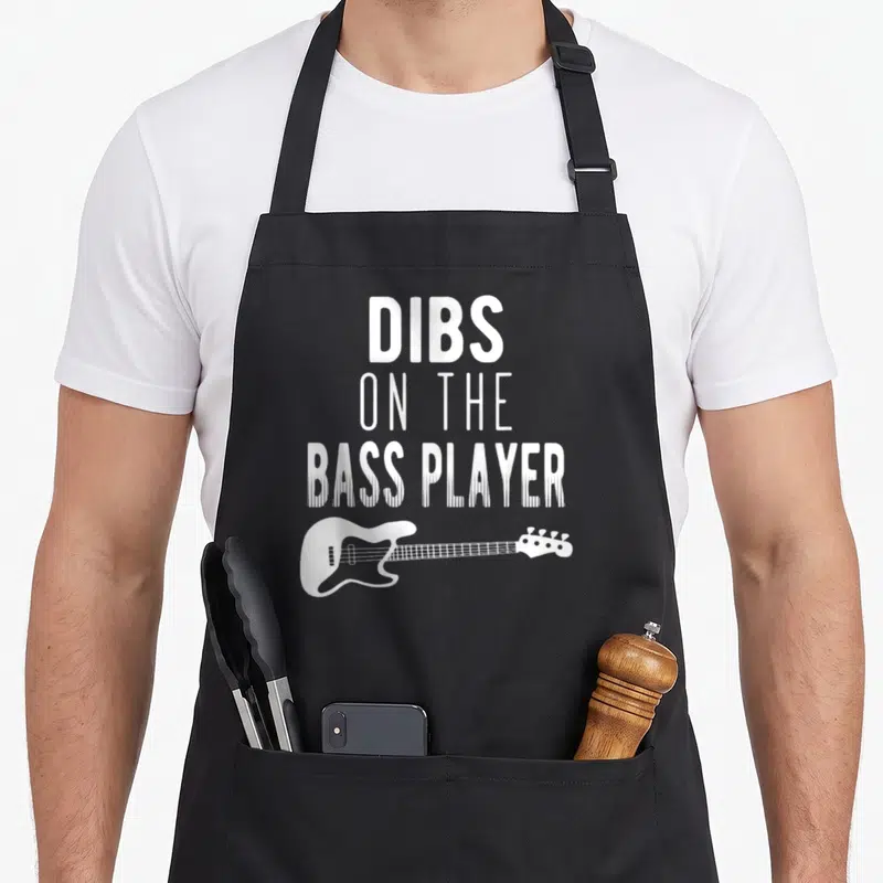 Dib bassist apron - White DIBS ON THE BASS PLAYER text stacked above a bass guitar silhouette — shown on a black cotton canvas apron against a white background