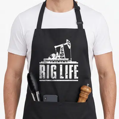 Field rig girl apron - White distressed oil pump silhouette above RIG LIFE text — shown on a black cotton canvas apron against a white background
