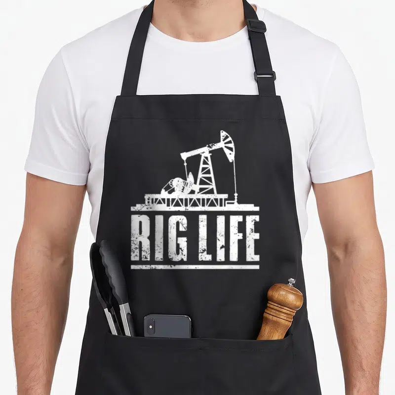 Field rig girl apron - White distressed oil pump silhouette above RIG LIFE text — shown on a black cotton canvas apron against a white background
