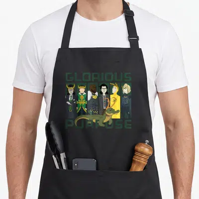 Variant purpose of apron - Loki variants in six panels with green alligator and text Glorious Purpose — shown on a black cotton canvas apron against a white background