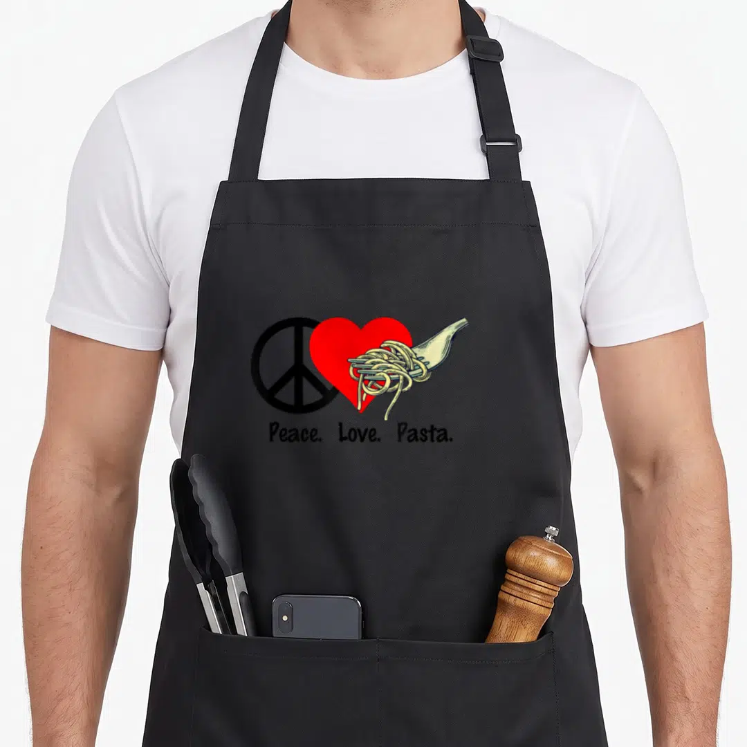 Peace pasta apron - Black peace sign, red heart, and cream pasta fork with text below — shown on a black cotton canvas apron against a white background