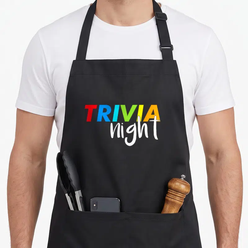 Trivia game aprons - Stacked TRIVIA night text in colorful block letters and white script — shown on a black cotton canvas apron against a white background