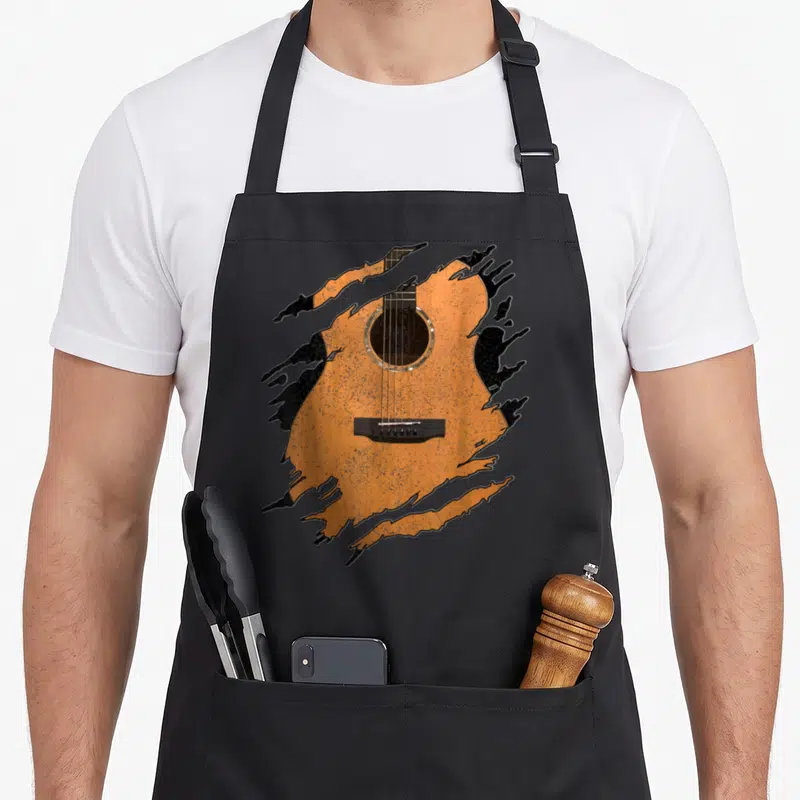Music acoustics apron - Orange acoustic guitar illustration framed by black paint splatters on black bib apron — shown on a black cotton canvas apron against a white background