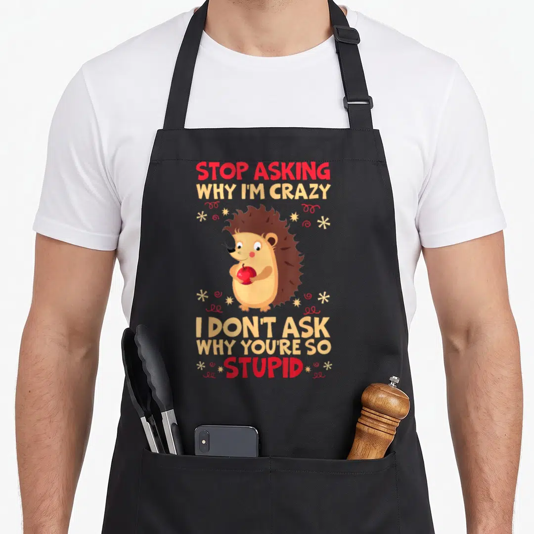 Asking crazy hedgehog lady apron - Cartoon hedgehog holding red apple with text stop asking why im crazy i dont ask why — shown on a black cotton canvas apron against a white background
