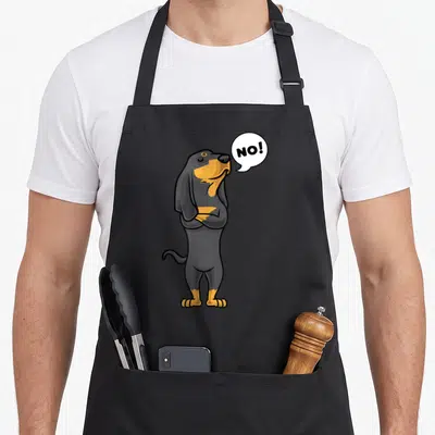 Stubborn coonhound dog apron - Cartoon black and tan dachshund standing with arms crossed next to a speech bubble — shown on a black cotton canvas apron against a white background