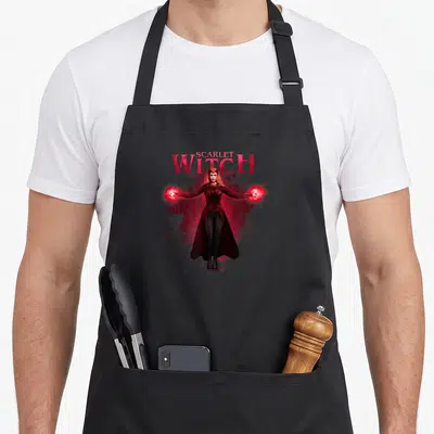 Scarlet doctor apron - Realistic Scarlet Witch figure with red energy orbs and stacked red text over a geometric symbol — shown on a black cotton canvas apron against a white background