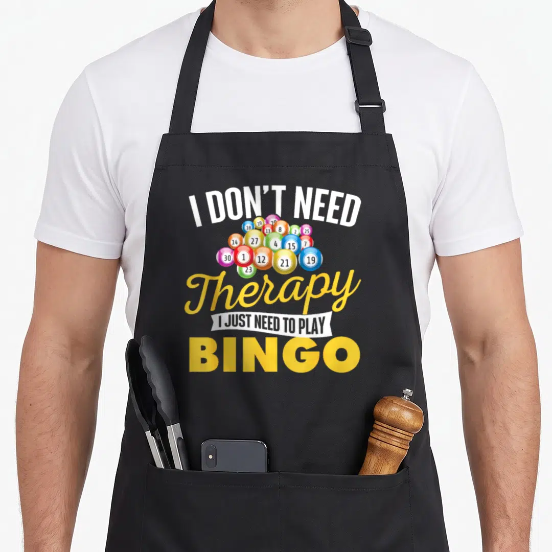 Gambler bingo apron - Stacked text I Don't Need Therapy above a cluster of multicolored numbered bingo balls — shown on a black cotton canvas apron against a white background