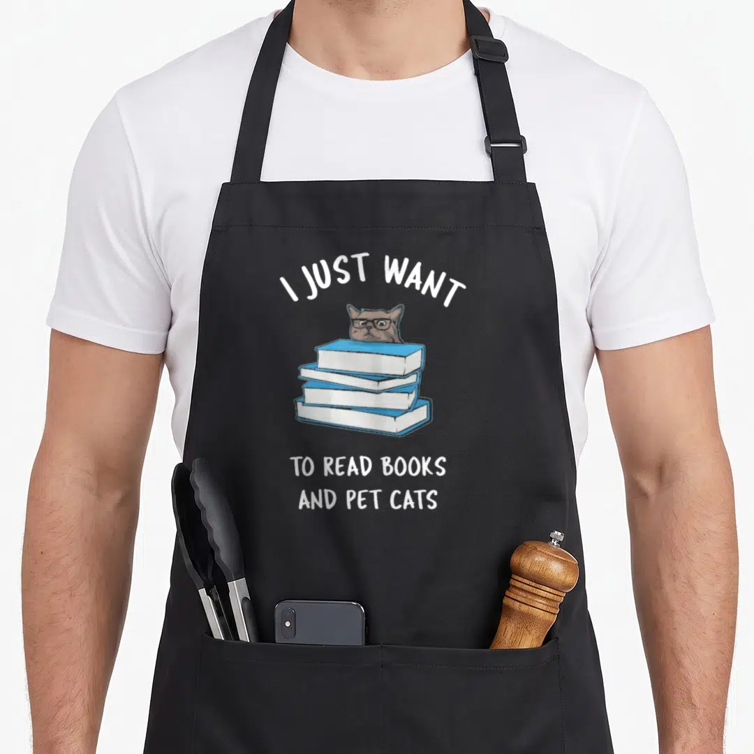 Read russian aprons - Cartoon brown cat with glasses peeking from behind three blue books with white text — shown on a black cotton canvas apron against a white background