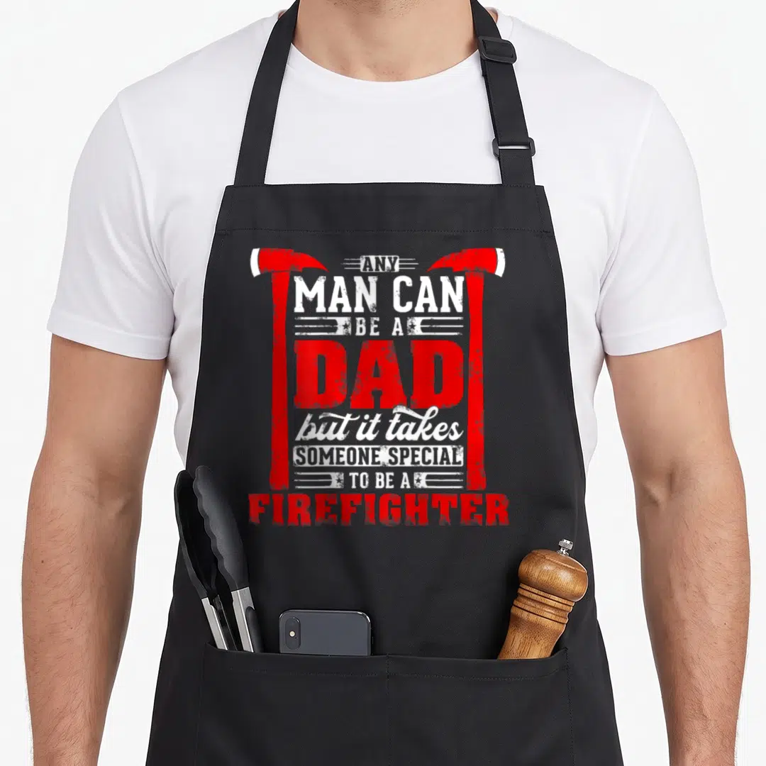 Special firefighter apron - Red and white stacked text reading any man can be a dad framed by two axes — shown on a black cotton canvas apron against a white background