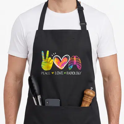 Peace radiology apron - Tie-dye peace hand, heart, and rib cage symbols above white text PEACE LOVE RADIOLOGY — shown on a black cotton canvas apron against a white background