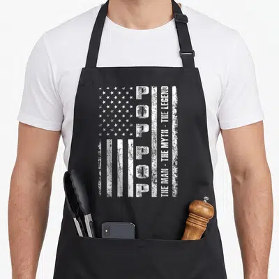 Pop us aprons - Distressed white US flag shape with vertical POP text and The Man The Myth The Legend inscription — shown on a black cotton canvas apron against a white background