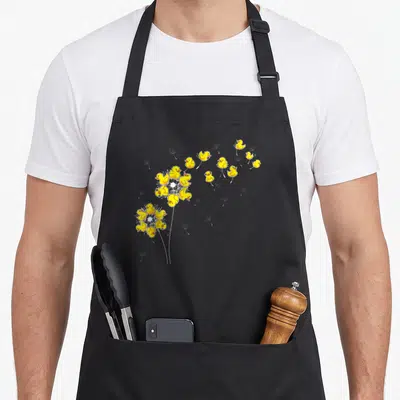 Dandelion duck apron - Yellow rubber ducks arranged as dandelion seeds blowing from white stems in cartoon style — shown on a black cotton canvas apron against a white background