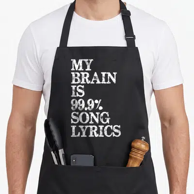 Brain music lovers apron - White stacked text reading My Brain Is 99.9% Song Lyrics on black background — shown on a black cotton canvas apron against a white background