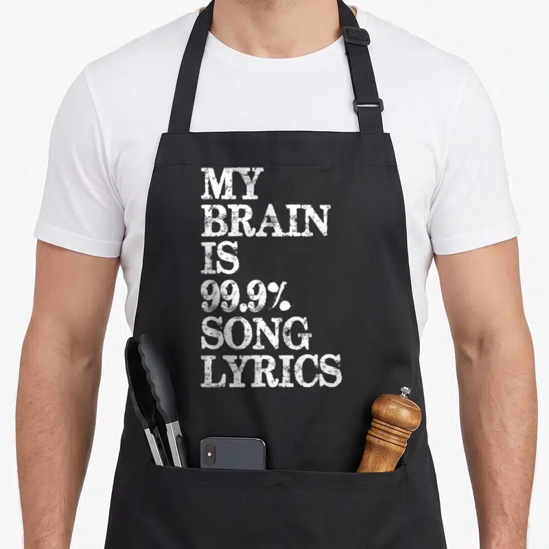 Brain music lovers apron - White stacked text reading My Brain Is 99.9% Song Lyrics on black background — shown on a black cotton canvas apron against a white background