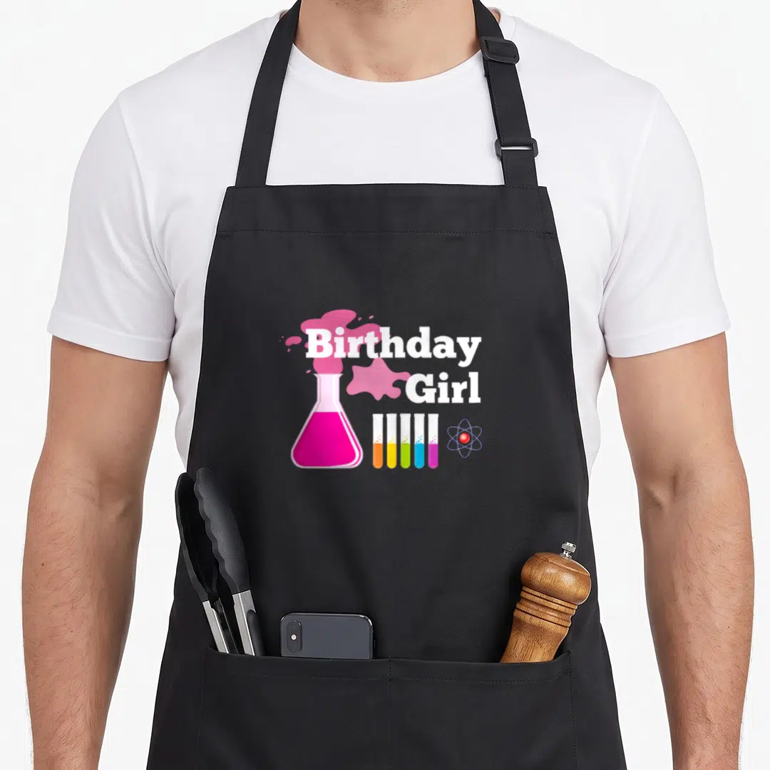 Mad science apron - Birthday Girl text with pink flask, four test tubes, and atom symbol in cartoon style — shown on a black cotton canvas apron against a white background