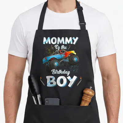 Mama truck apron - Monster truck graphic with MOMMY Of the Birthday BOY text and exhaust pipes — shown on a black cotton canvas apron against a white background