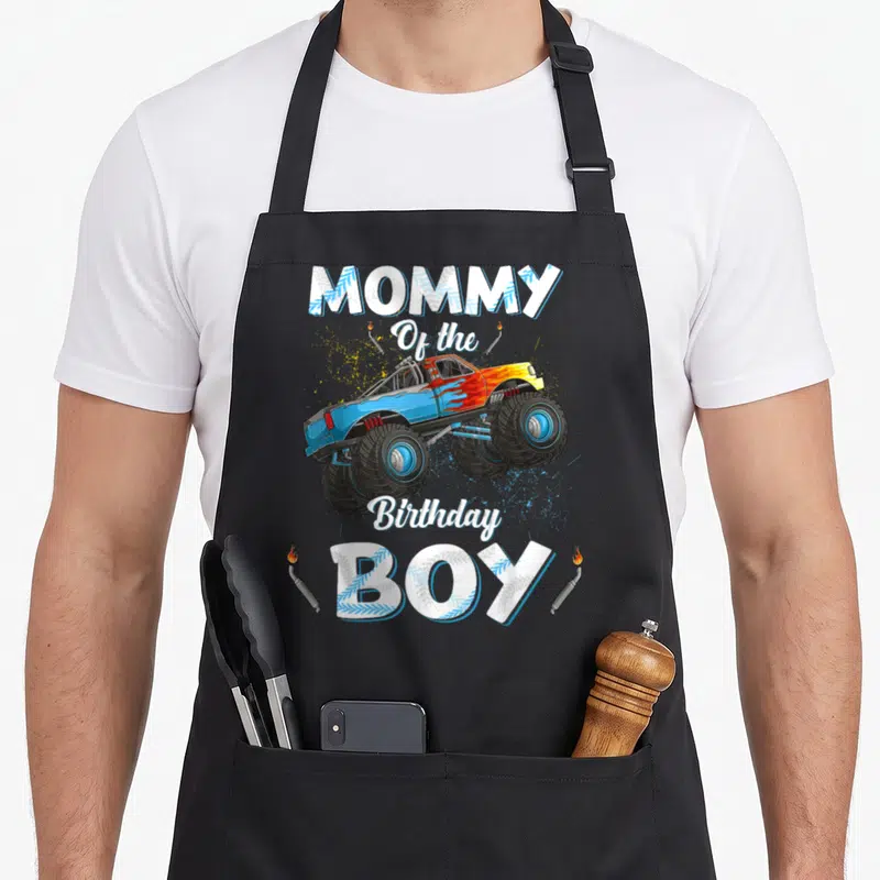 Mama truck apron - Monster truck graphic with MOMMY Of the Birthday BOY text and exhaust pipes — shown on a black cotton canvas apron against a white background
