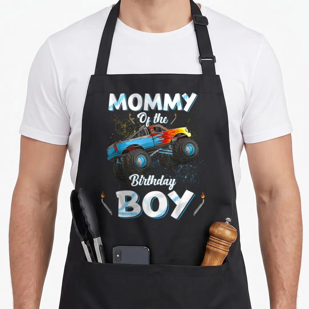 Mama truck apron - Monster truck graphic with MOMMY Of the Birthday BOY text and exhaust pipes — shown on a black cotton canvas apron against a white background