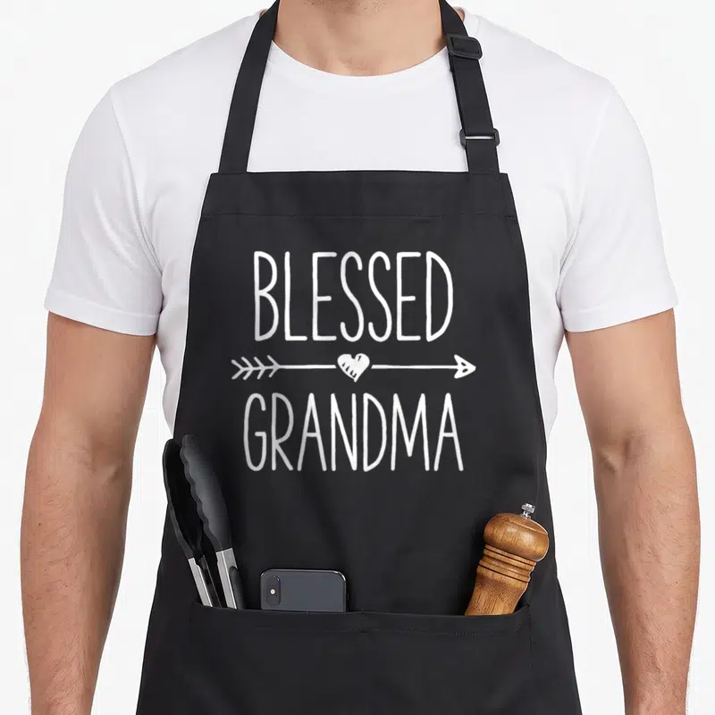 Blessed mother's apron - White BLESSED GRANDMA text with arrow and heart graphic — shown on a black cotton canvas apron against a white background