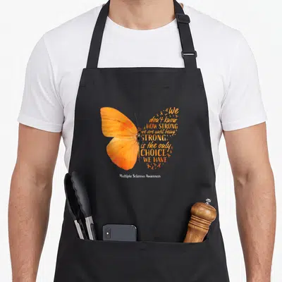 Sclerosis butterfly apron - Realistic orange butterfly with text forming right wing and small ribbons, white text below — shown on a black cotton canvas apron against a white background