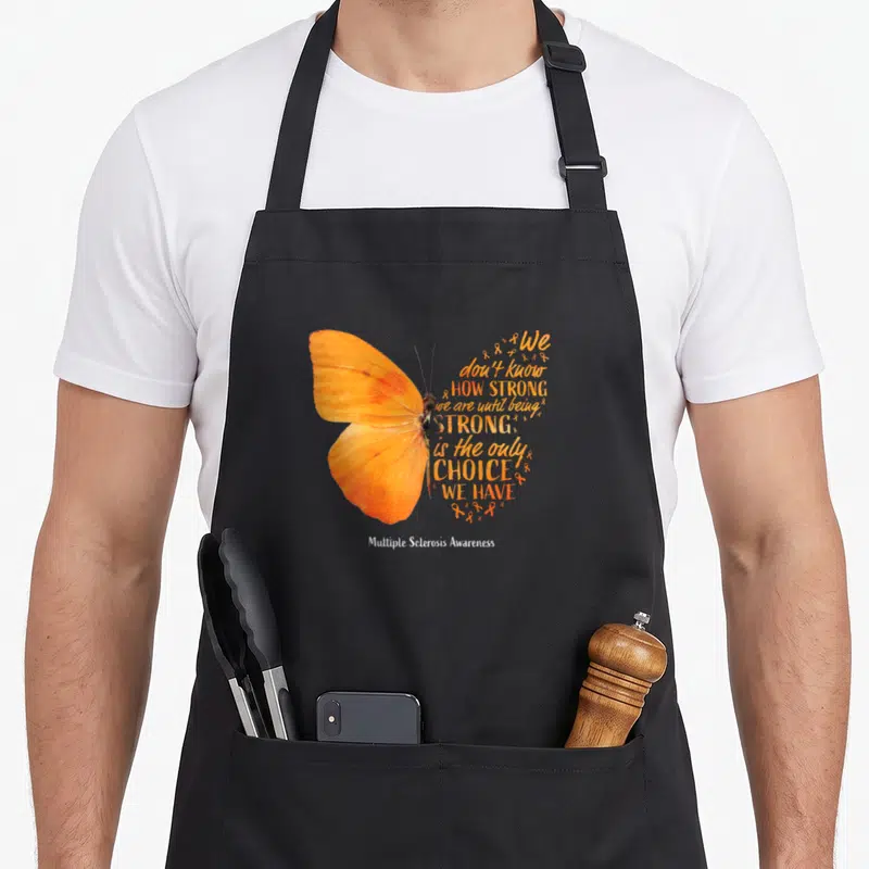Sclerosis butterfly apron - Realistic orange butterfly with text forming right wing and small ribbons, white text below — shown on a black cotton canvas apron against a white background