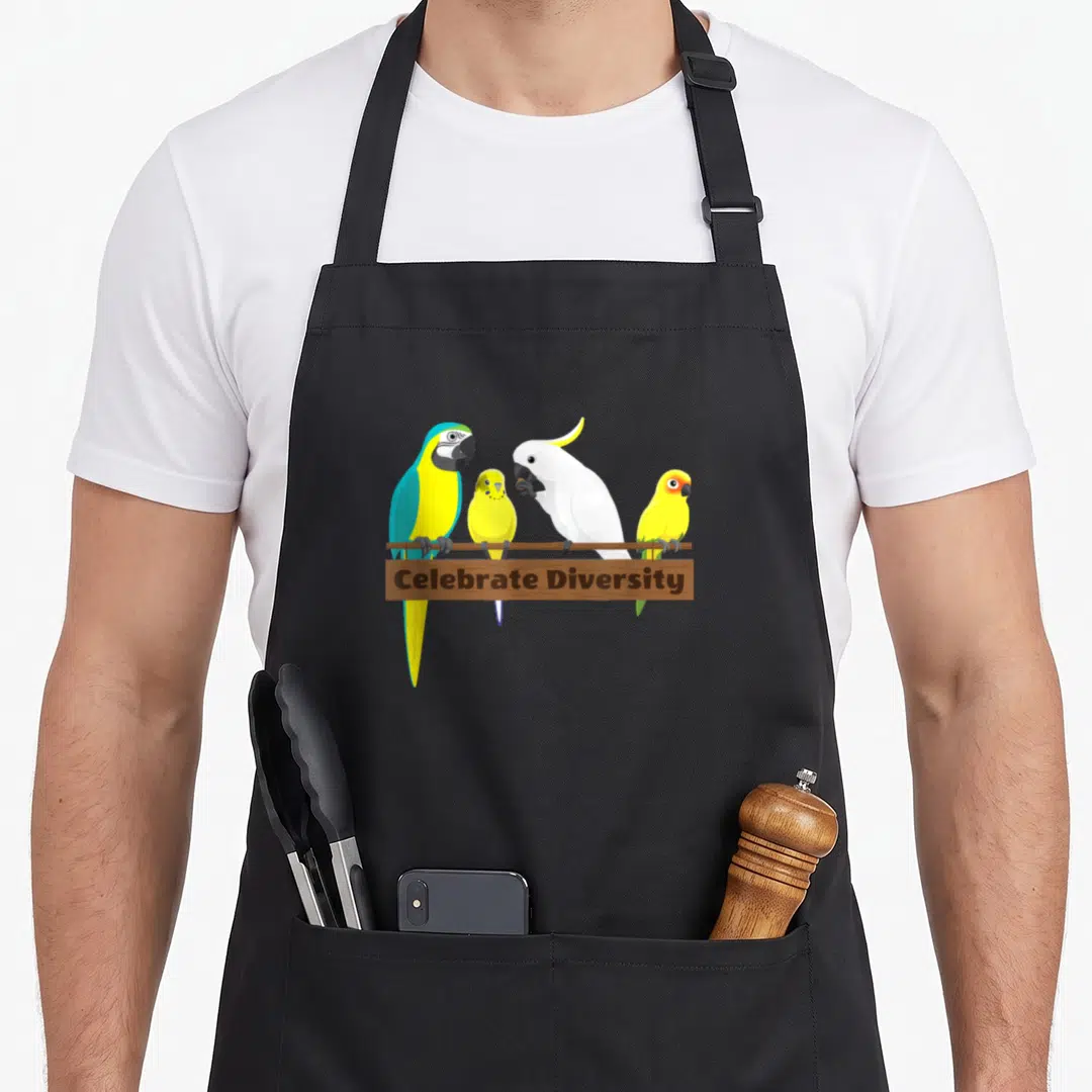 Celebrate parrot apron - Four parrots perched on a brown bar above a wooden sign reading Celebrate Diversity in cartoon — shown on a black cotton canvas apron against a white background
