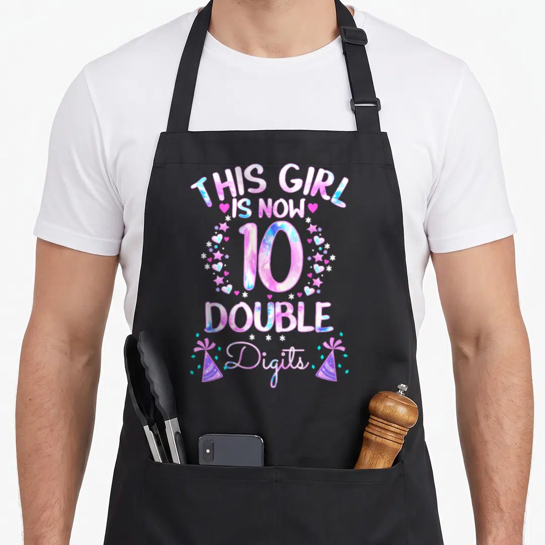 Tie double apron - THIS GIRL IS NOW 10 DOUBLE DIGITS text with hearts stars and party hats — shown on a black cotton canvas apron against a white background