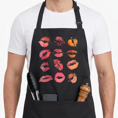 Kissing graphic wife apron - Twelve red, orange, and pink watercolor lip prints in a 4x3 grid — shown on a black cotton canvas apron against a white background
