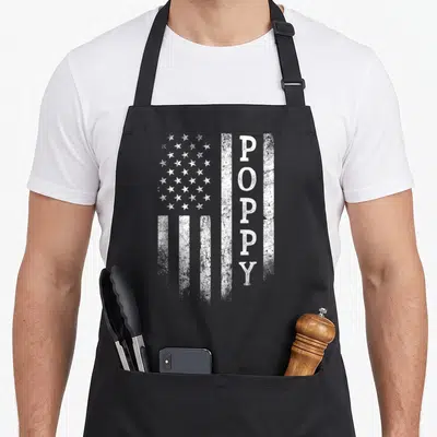 Poppy flag father day apron - Distressed white USA flag with vertical POPPY text replacing a stripe — shown on a black cotton canvas apron against a white background