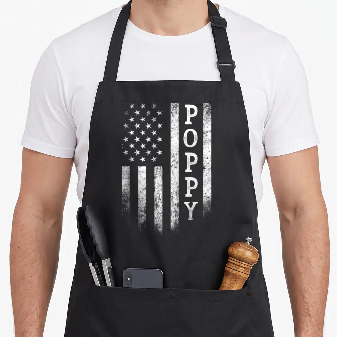 Poppy flag father day apron - Distressed white USA flag with vertical POPPY text replacing a stripe — shown on a black cotton canvas apron against a white background