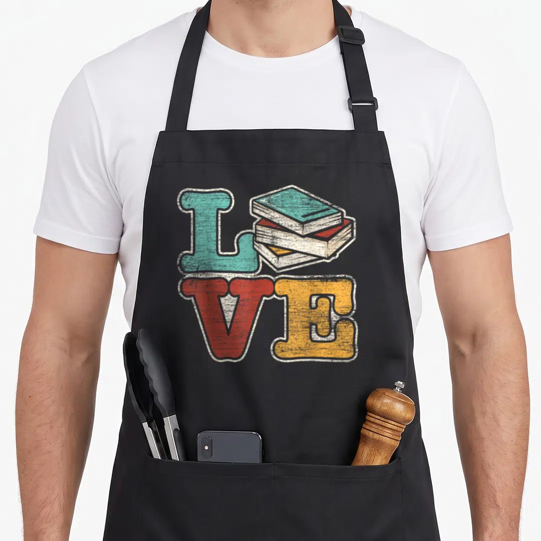 Reader reading book apron - Retro LOVE text with stacked books replacing the O in teal, red, and yellow — shown on a black cotton canvas apron against a white background
