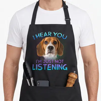 Hear beagle apron - Brown and white dog photo with blue and purple text I HEAR YOU I'M JUST NOT LISTENING — shown on a black cotton canvas apron against a white background