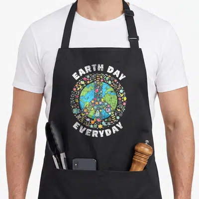 Earth everyday apron - Cartoon Earth surrounded by flowers, leaves, and birds with EARTH DAY EVERYDAY text — shown on a black cotton canvas apron against a white background