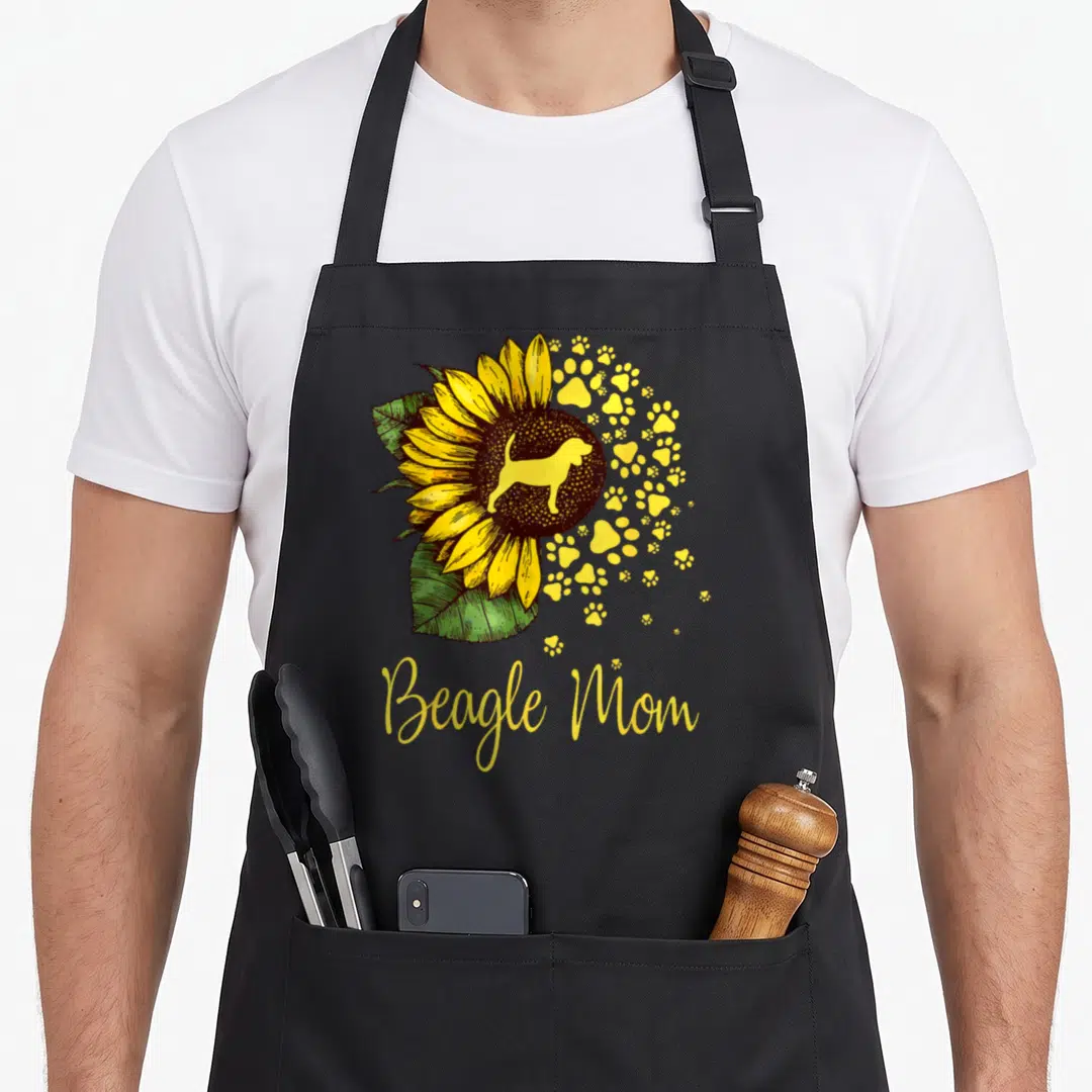 Sunflower beagle apron - Beagle Mom text below sunflower with dog silhouette and scattered yellow paw prints — shown on a black cotton canvas apron against a white background