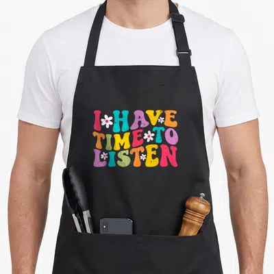 Mental suicide prevention apron - Retro colorful text I HAVE TIME TO LISTEN with white flowers on black bib — shown on a black cotton canvas apron against a white background